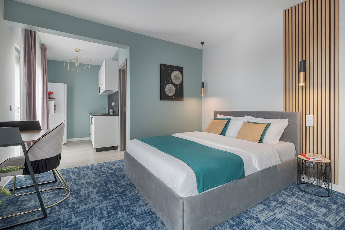A modern hotel room with a large bed, a desk, and a kitchenette.