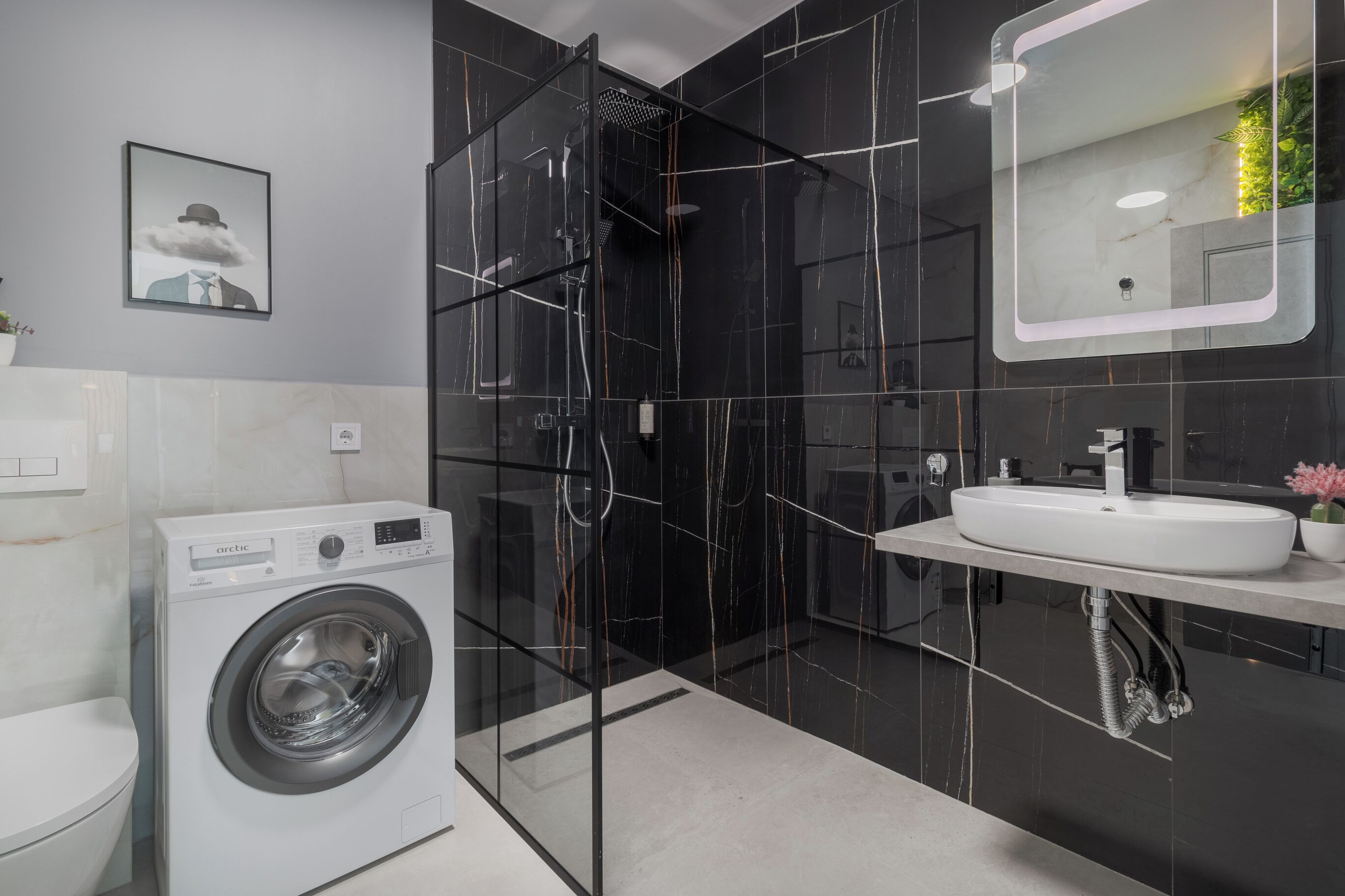 A modern bathroom with a black marble shower, a white sink, and a front-loading washing machine.