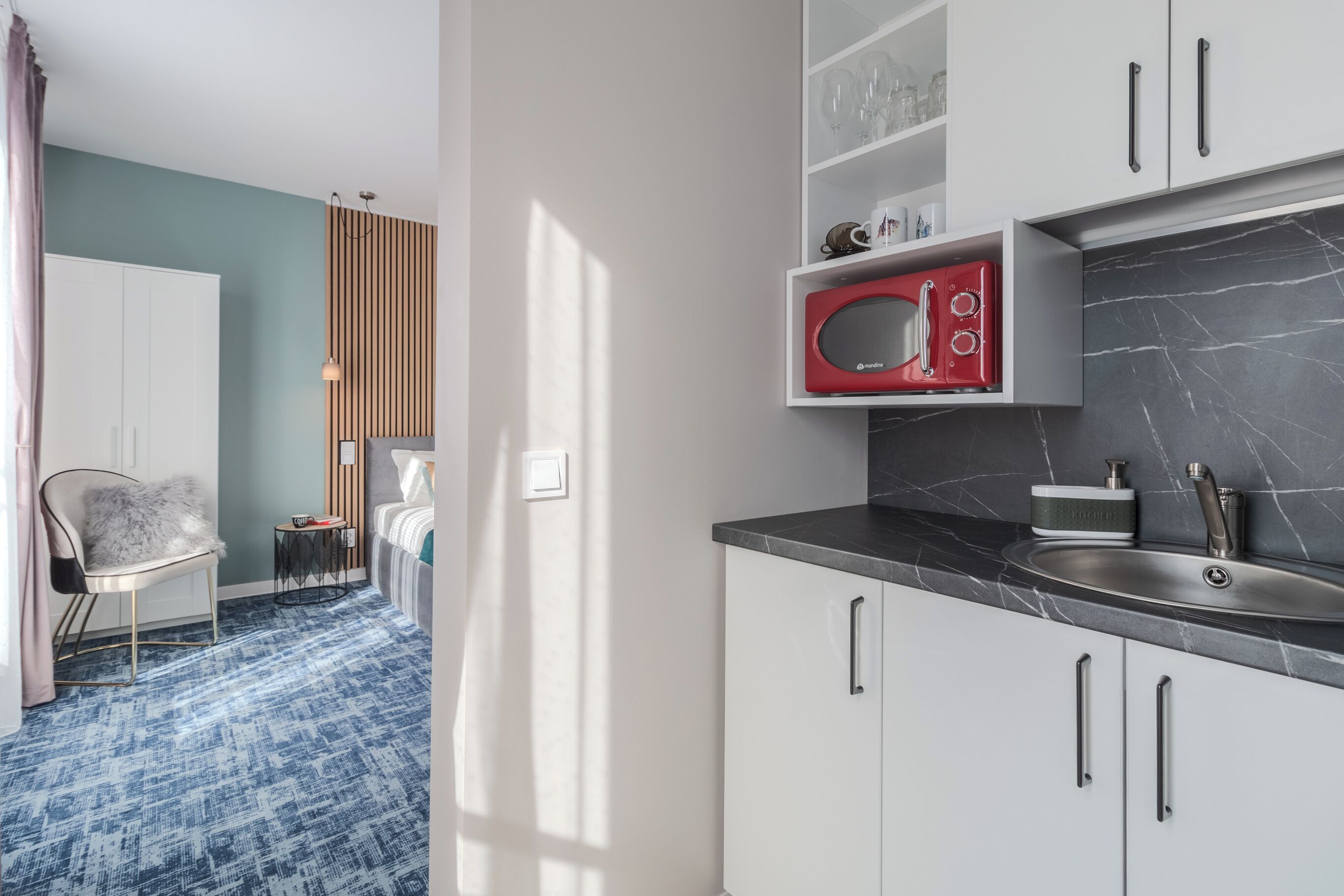 A modern kitchen with white cabinets, a red microwave, and a marble countertop.