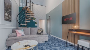 Ein modernes Wohnzimmer mit grauem Sofa, rundem Couchtisch, Schreibtisch aus Holz und einem Netflix-Schild an der Wand.