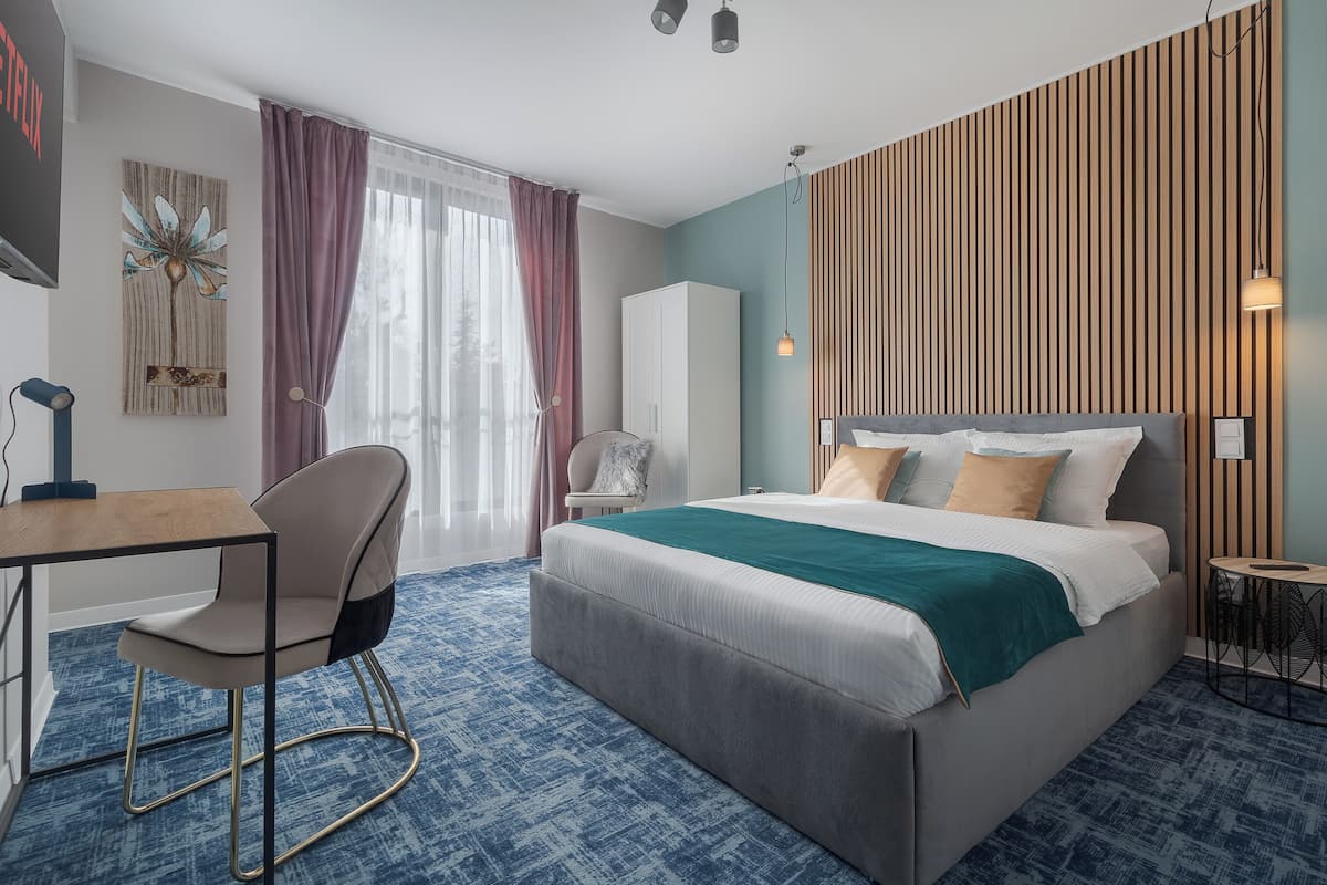 A modern hotel room with a bed, desk, chair, and a view of the outdoors.