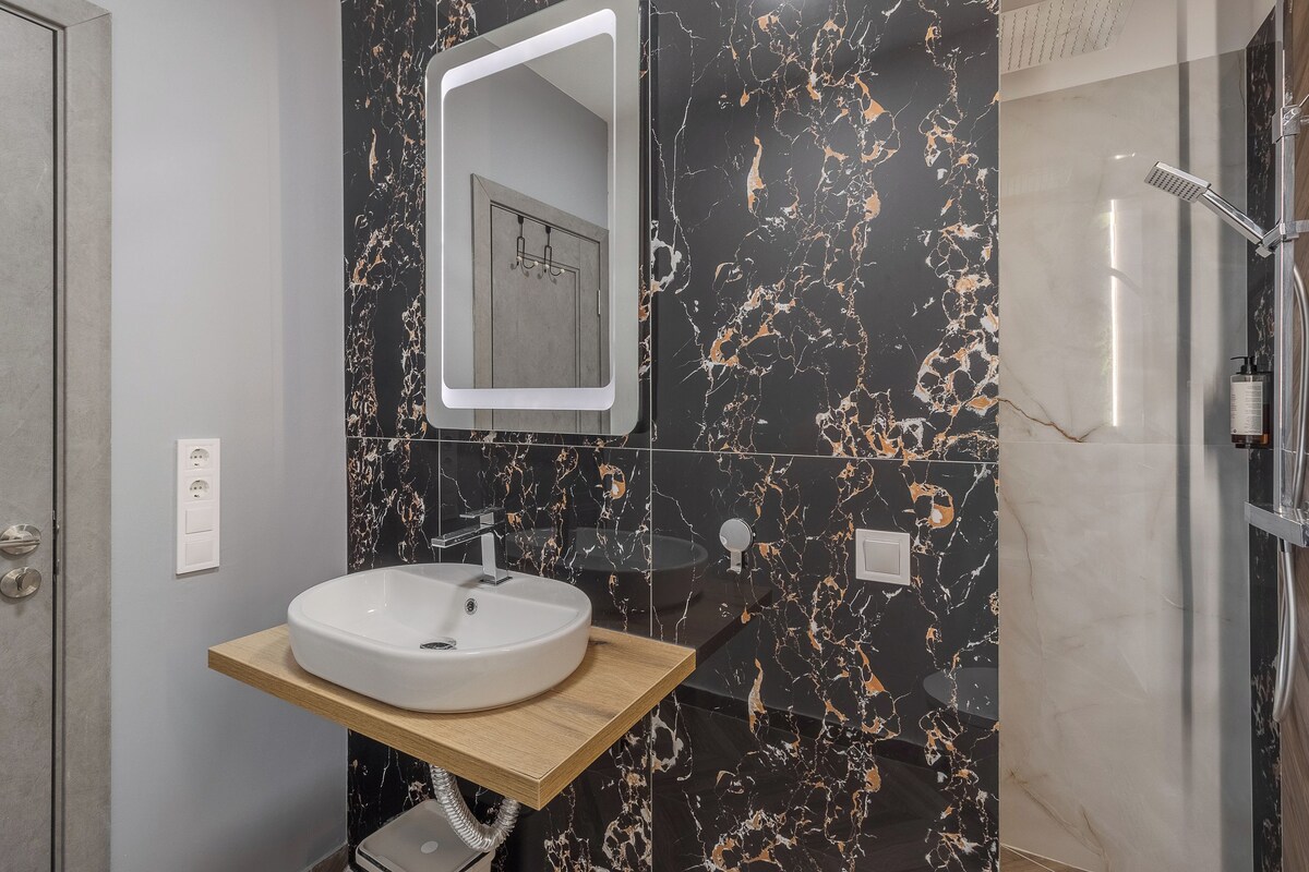 Un baño moderno con salpicadero de mármol, tocador de madera, lavabo redondo, espejo y zona de ducha.