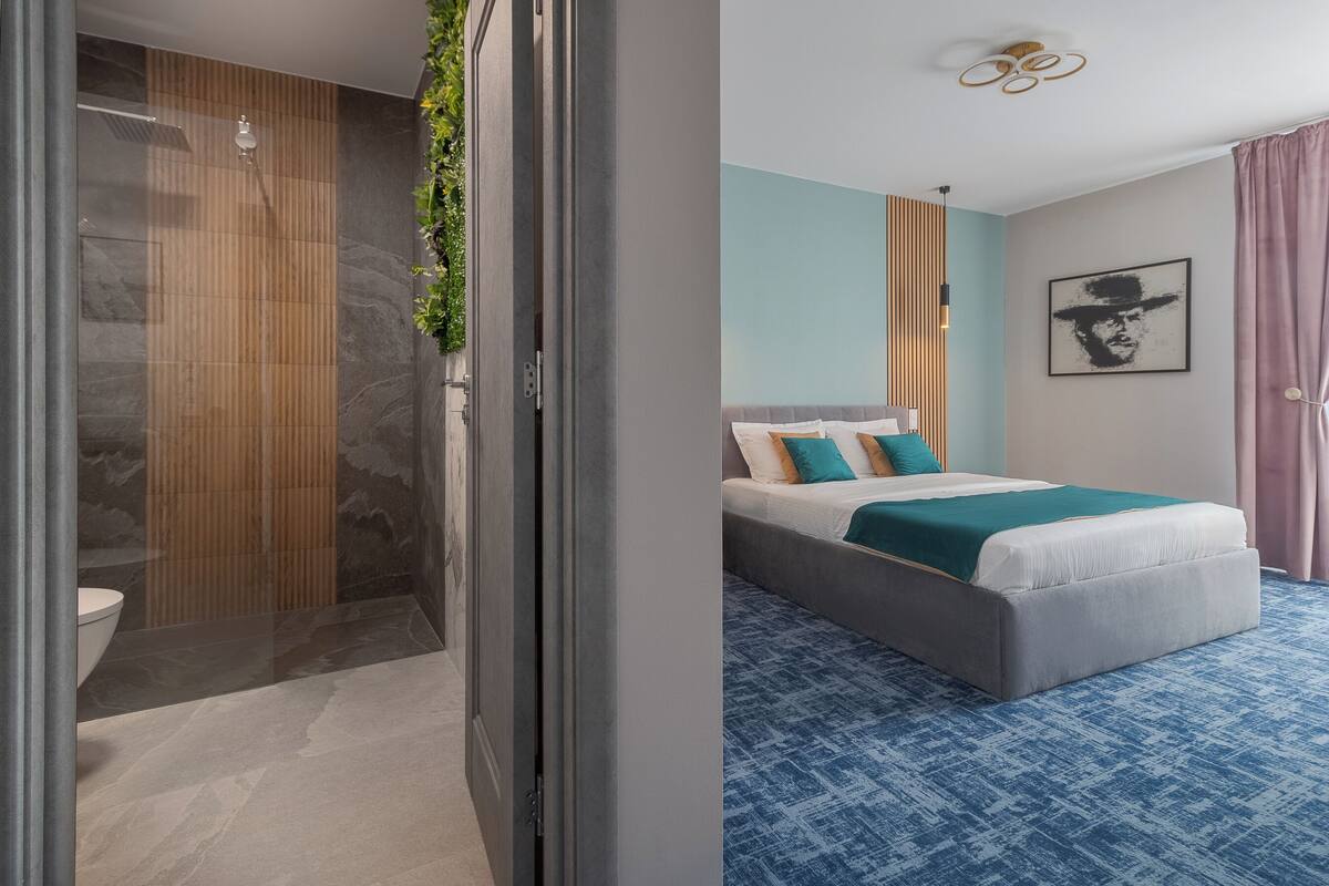 A modern hotel room with a shower, a bed with a blue and white color scheme, and a framed picture on the wall.