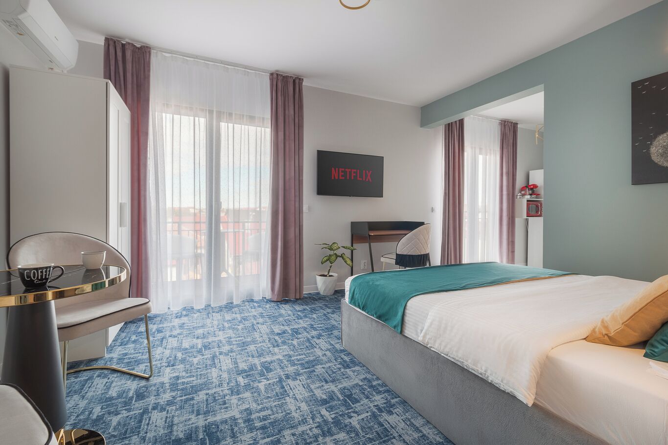 A hotel room with a bed, a desk, a chair, a coffee table, and a TV displaying 'NETFLIX'.