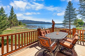 A wooden deck with a round table and chairs, overlooking a lake with boats and mountains in the background. - Lakefront Chalet near Village and Slopes (Big Bear)