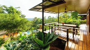 Eine Holzterrasse mit Pool, umgeben von üppiger Vegetation und Blick auf ferne Hügel.