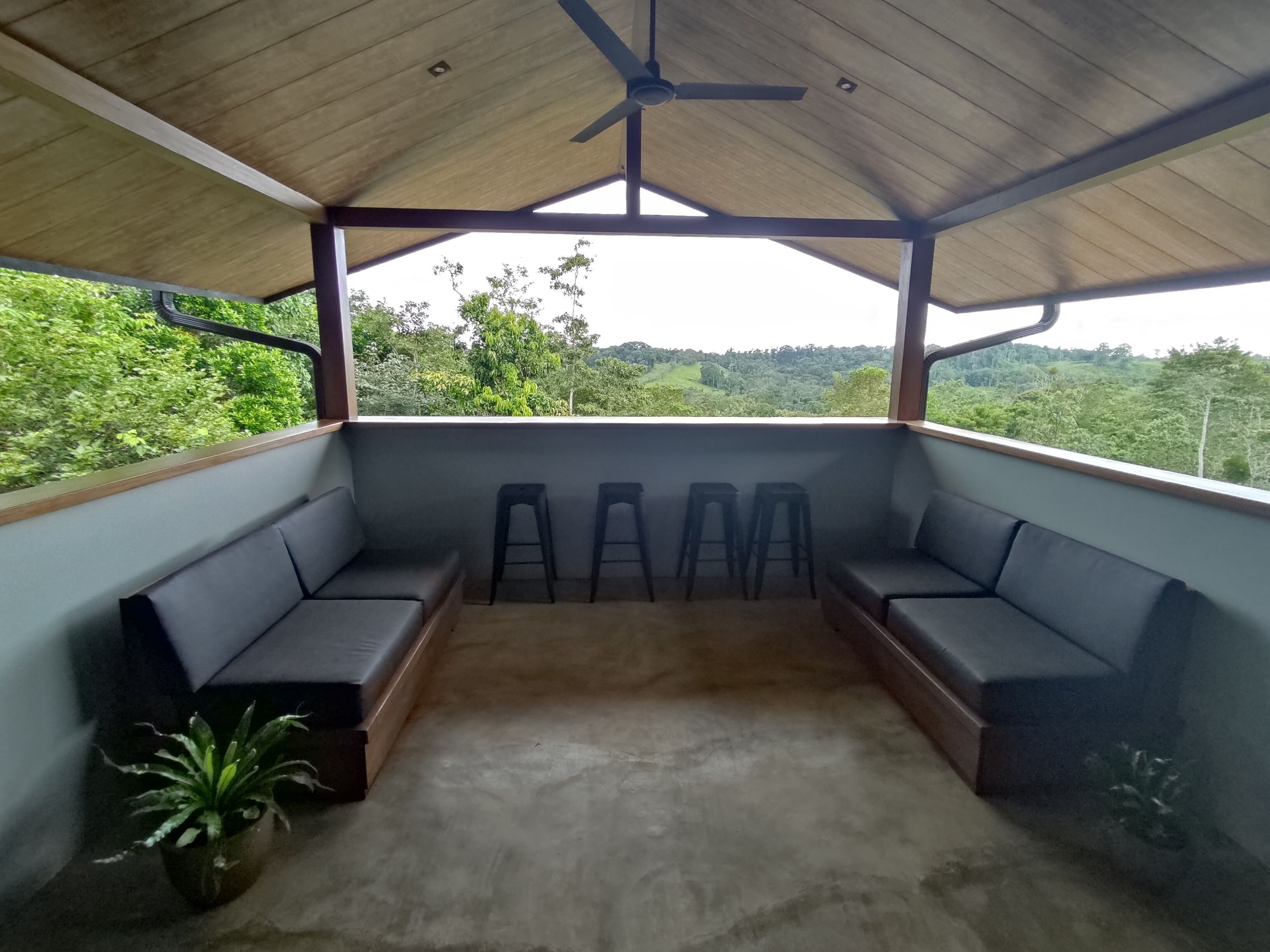 A covered outdoor seating area with a ceiling fan, benches, and potted plants.