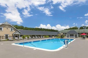 A swimming pool with lounge chairs and a covered area, surrounded by buildings.