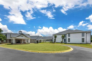 A building with a covered entrance, a lawn, and a curved driveway.