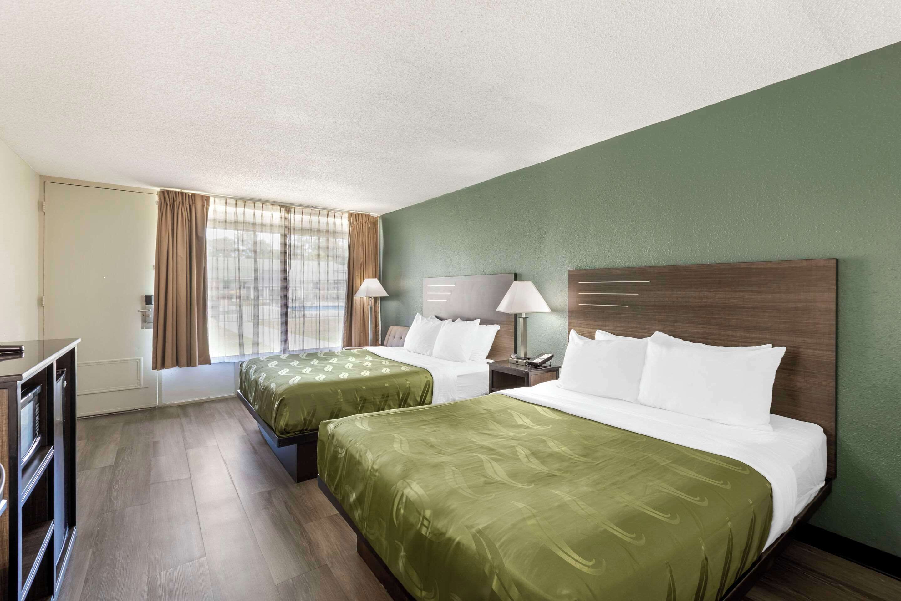 Une chambre d’hôtel avec deux lits, un bureau et une fenêtre avec des rideaux.