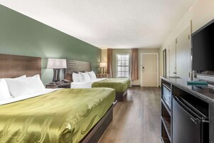 A hotel room with two beds, a TV, a desk, and a minibar.
