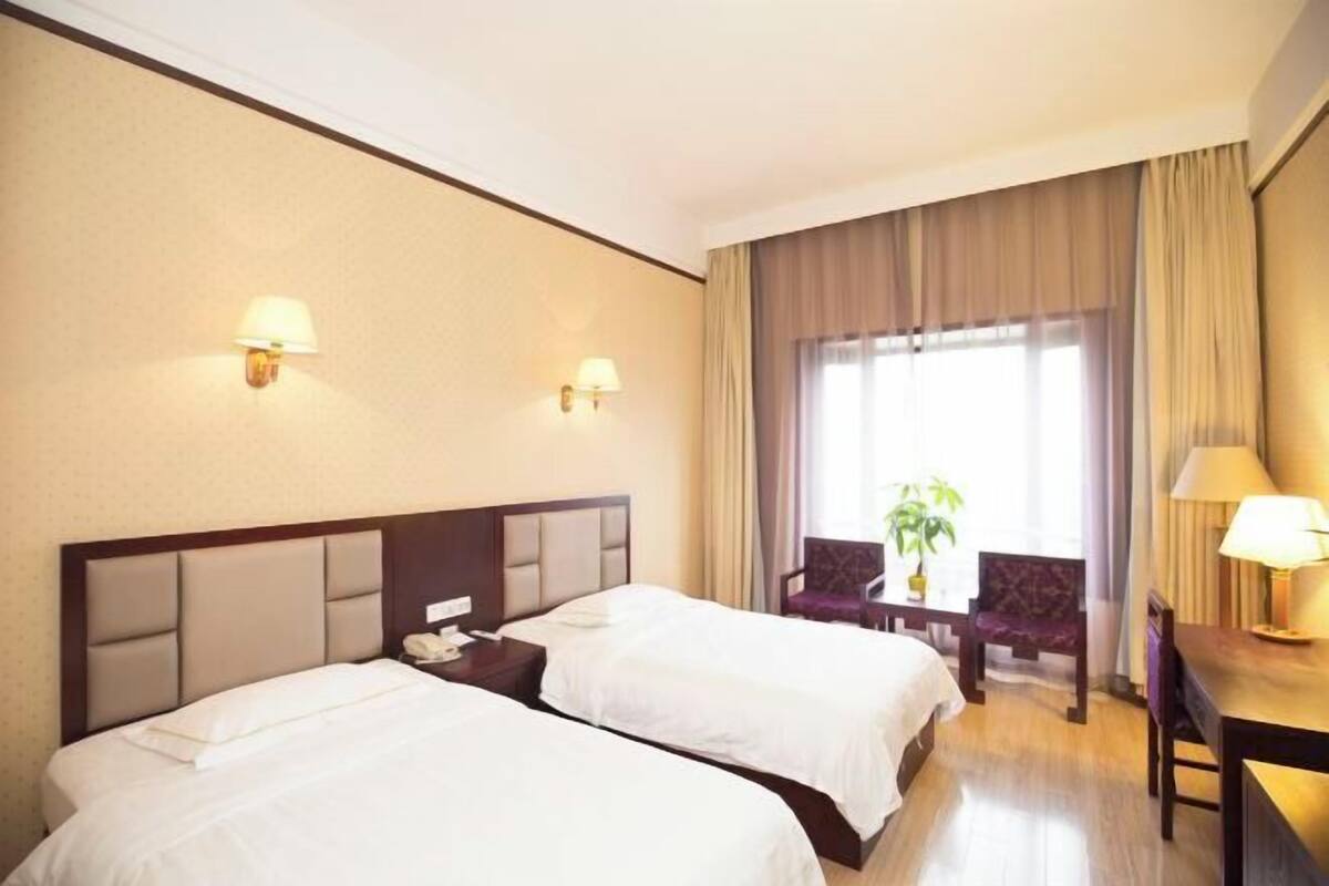 Ein Hotelzimmer mit zwei Betten, einem Schreibtisch, einem Stuhl und einem Vorhangfenster.
