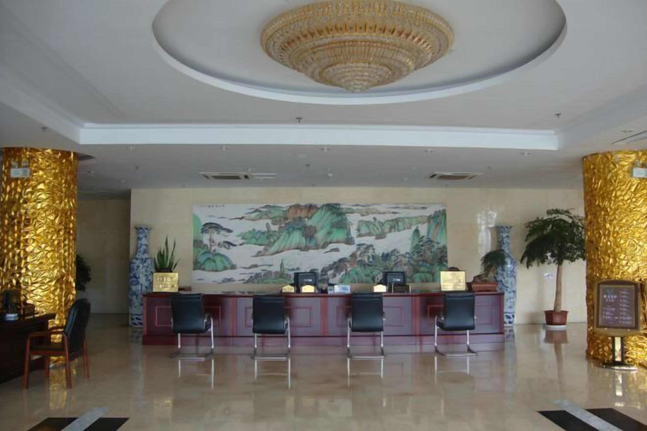 A hotel reception area with a large mural, a chandelier, and golden decorative columns.
