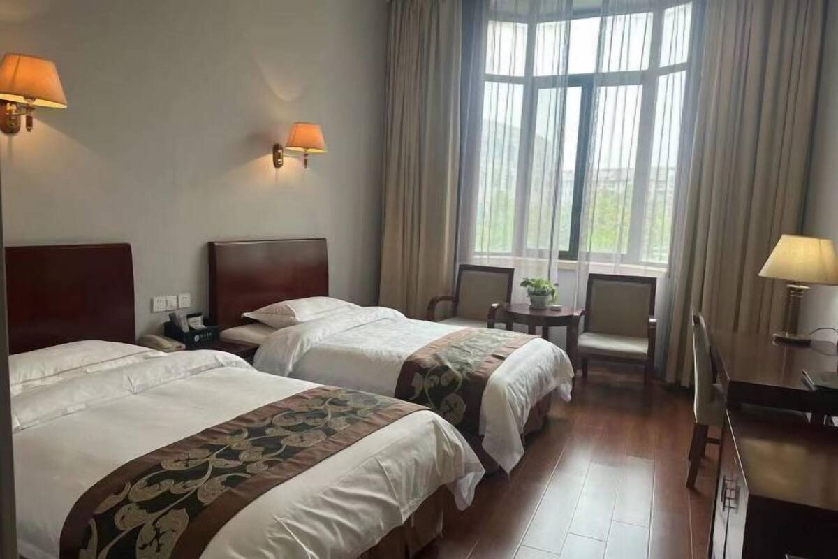 Ein Hotelzimmer mit zwei Betten, einem Schreibtisch, einem Stuhl und einem Fenster mit Vorhängen.