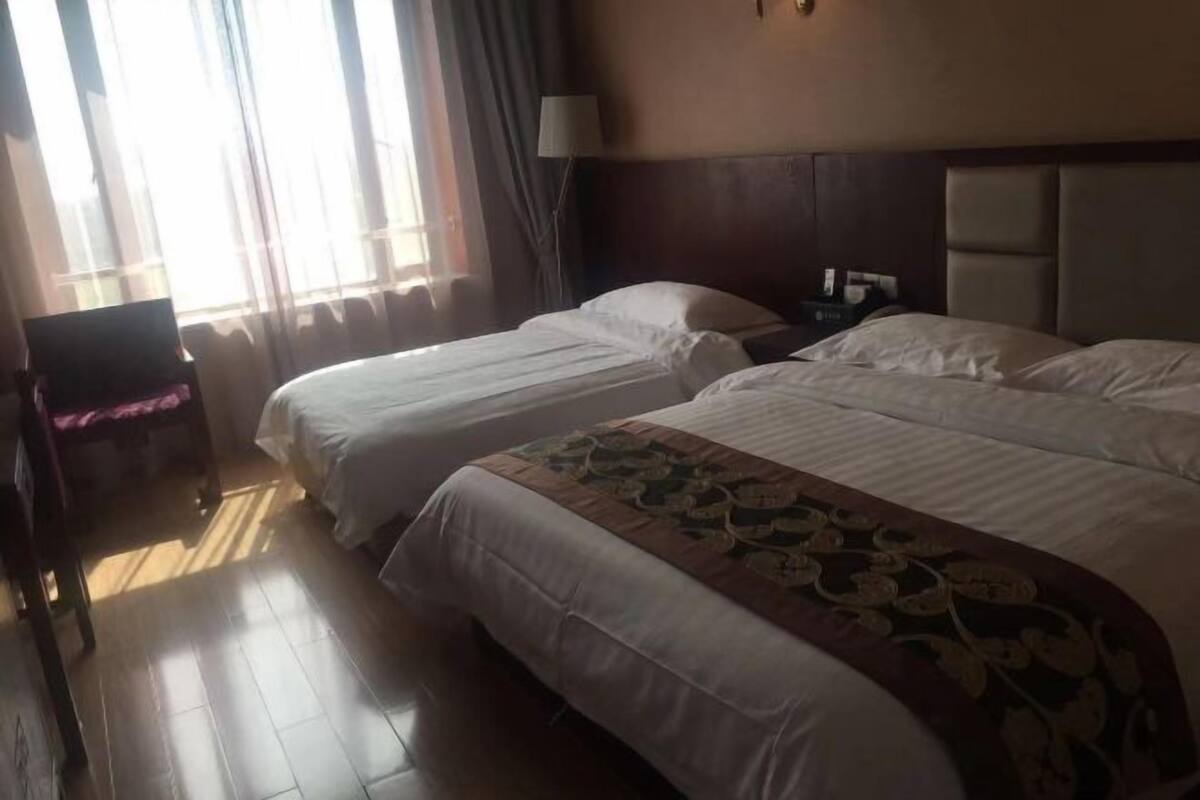 Ein Hotelzimmer mit zwei Betten, einem Nachttisch, einer Lampe und einem Fenster mit Vorhängen.