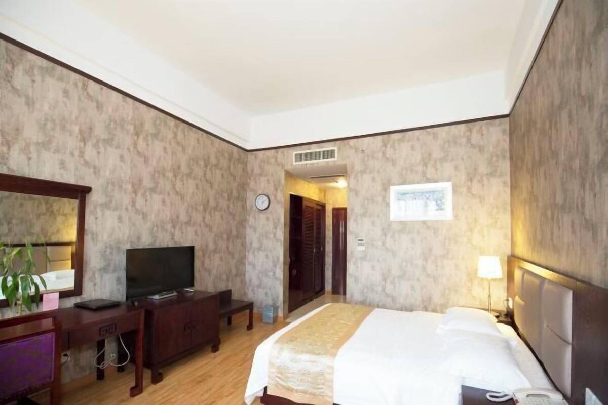 Ein Hotelzimmer mit einem Bett, einem Schreibtisch mit Fernseher, einer Schreibtischlampe und einer Wanduhr.