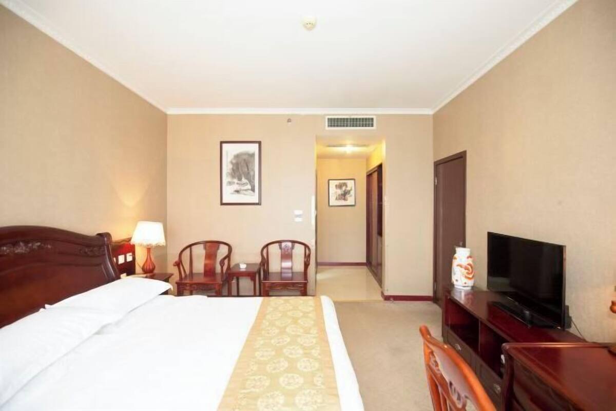 Ein Hotelzimmer mit einem Bett, einem Fernseher, einem Schreibtisch mit Stühlen und gerahmten Bildern an der Wand.