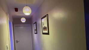 A hallway with a white door at the end, two hanging pendant lights, and two framed pictures on the wall. - 1 Bed Flat - Sleeps 2 - Hot Tub - Parking - Wifi (Bradford)