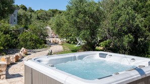 A hot tub surrounded by greenery, a stone pathway, and a building in the background.