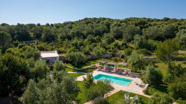 A large house with a swimming pool, surrounded by lush greenery and hills.