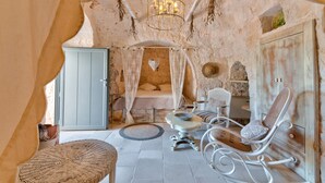 A rustic bedroom with a stone wall, a canopy bed, a wooden wardrobe, and a wicker chair. - Pigreco 6+2, Emma Villas (Ostuni)
