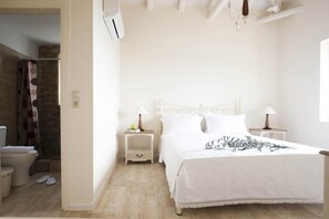 Une chambre à coucher comprenant un lit, deux tables de chevet, une commode, une fenêtre et une salle de bain avec des toilettes et un rideau de douche.