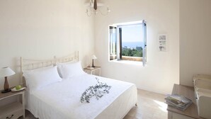 Une chambre à coucher avec un lit, une table de chevet avec une lampe, une fenêtre donnant sur un paysage dégagé et une petite table avec un livre.