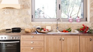 Une cuisine avec un mur en pierre, des placards en bois, une cuisinière, un évier et une fenêtre donnant sur des arbres.