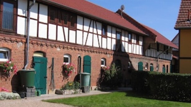 Un bâtiment traditionnel à colombages, avec un toit rouge, des portes vertes et des jardinières sur les rebords des fenêtres.