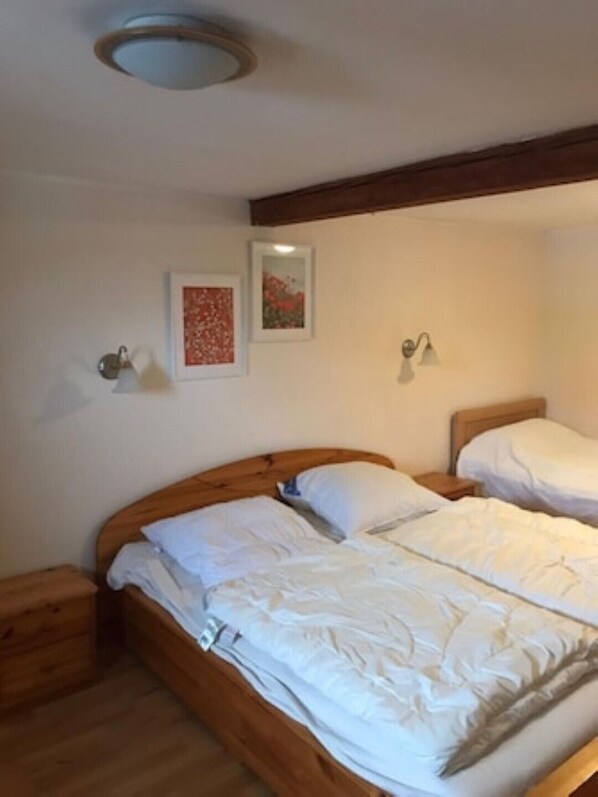 Cama doble con cabecera de madera, ropa de cama blanca y dos mesitas de noche.