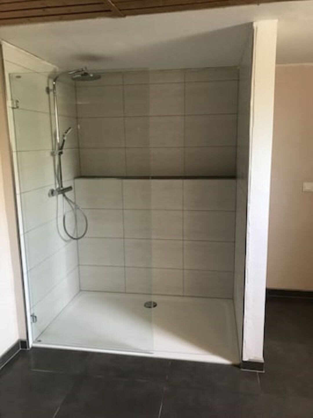 A shower with a glass door, tiled walls, and a dark floor.