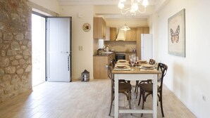 Een eethoek met een houten tafel voor zes personen, omringd door stoelen. Een stenen muur en een deur zijn links zichtbaar, die leiden naar een andere kamer.