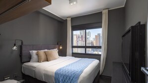 Habitación de hotel moderna con una cama grande, un televisor de pantalla plana y vistas a la ciudad a través de un amplio ventanal.