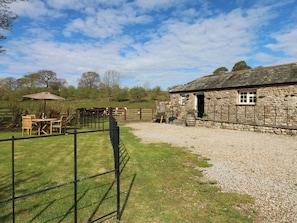 A stone building with a gravel driveway, a fenced outdoor seating area with chairs and a table, and a clear sky.