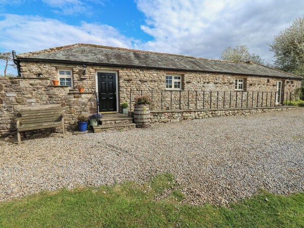 A stone building with a gravel driveway, a wooden bench, and a black door.