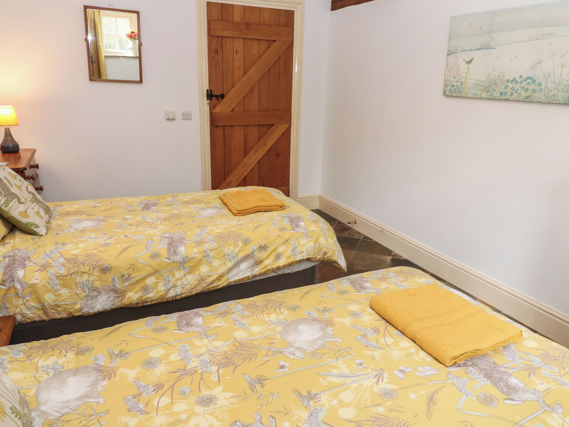 Una camera da letto con due letti, una porta in legno, un quadro appeso al muro e una lampada sul comodino.