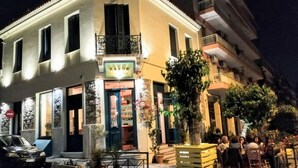 A corner building with a bar on the ground floor, potted plants, and a group of people outside. - Luxurious Minimal Apartment in Acropolis (Athens)