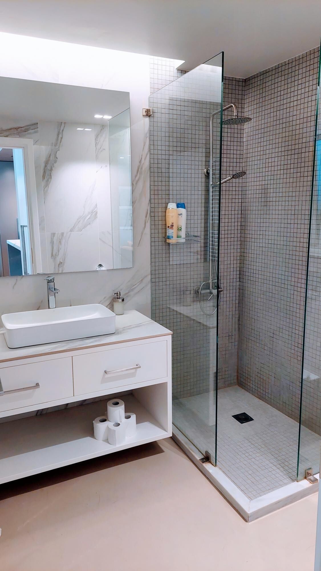 A modern bathroom with a glass-enclosed shower, a marble-tiled vanity, and a large mirror.