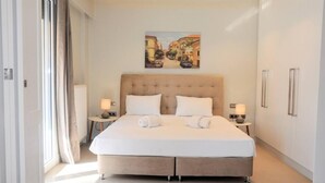 A modern hotel room with a large bed, two bedside tables with lamps, a headboard, and a painting of a street scene on the wall. - Luxurious Minimal Apartment in Acropolis (Athens)