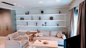 A modern living room with a sofa, a coffee table, and a TV. There are shelves with various decorative items and a wardrobe. - Luxurious Minimal Apartment in Acropolis (Athens)