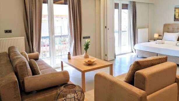 A modern hotel room with a sofa, armchairs, a small table, and a bed. - Luxurious Minimal Apartment in Acropolis (Athens)