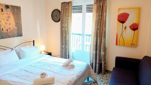 Ein Hotelzimmer mit Bett, Nachttisch, Lampe, Gemälde und Blick ins Freie.