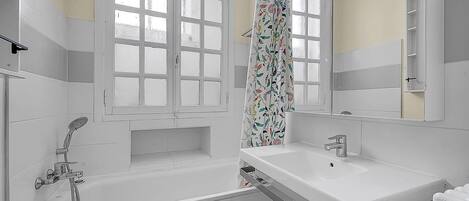 Un baño moderno con bañera, lavamanos, ducha y ventana con cortina.