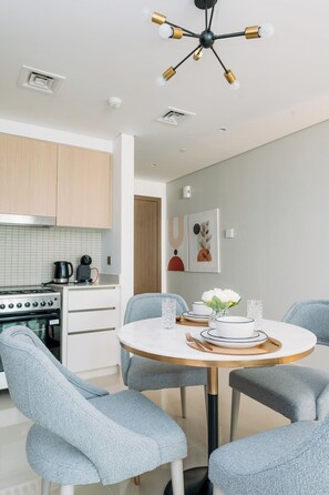 Une cuisine moderne équipée d’une cuisinière, d’un four et d’une machine à café, d’une table à manger avec des chaises et d’un luminaire au plafond.