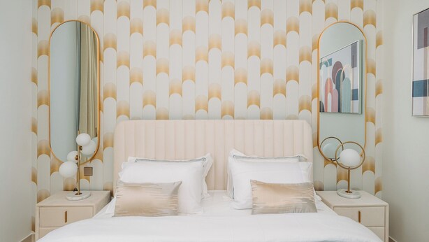 Une chambre avec un grand lit, deux tables de chevet et deux miroirs fixés au mur.