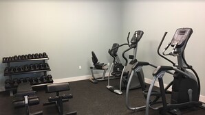 Une salle de sport équipée de tapis de course, d’haltères et d’un banc de musculation.