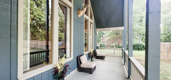 Eine überdachte Veranda mit zwei Korbstühlen und einem Blumentopf.