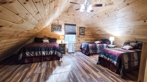 Um quarto de sótão acolhedor, com duas camas, paredes de madeira, um ventilador de teto e uma janela com persianas.