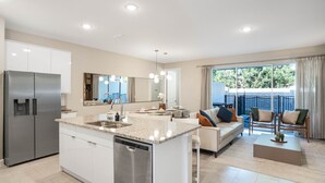 A modern kitchen with a dishwasher, a large island with a sink, and a dining area with a sofa and chairs. - Summer Specials - Super Close to Disney Parks +Restaurants + Heated Plunge Pool (Kissimmee)