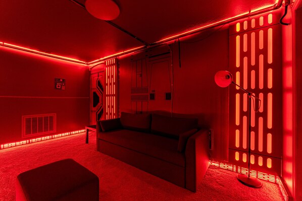 Una habitación iluminada en rojo, con un sofá, una mesita y una lámpara de pie.